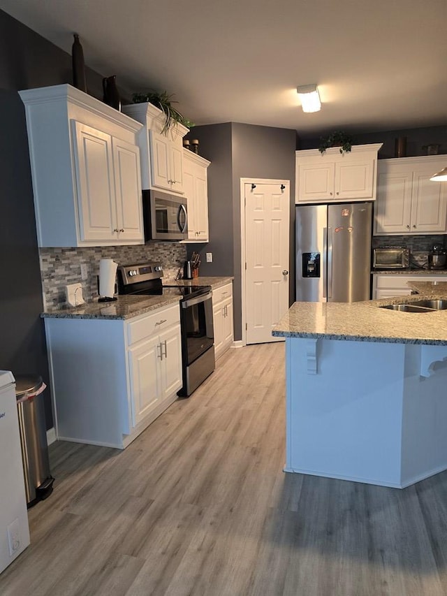 kitchen with backsplash, white cabinetry, stainless steel appliances, and light hardwood / wood-style flooring