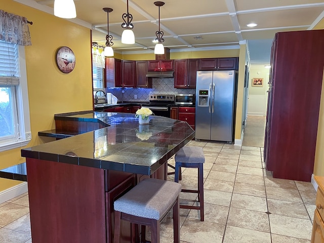 kitchen with a sink, dark brown cabinets, under cabinet range hood, appliances with stainless steel finishes, and tasteful backsplash