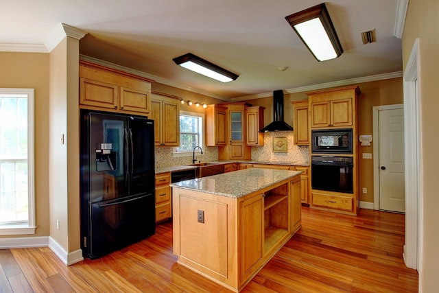 kitchen with tasteful backsplash, wall chimney exhaust hood, black appliances, light hardwood / wood-style flooring, and a center island