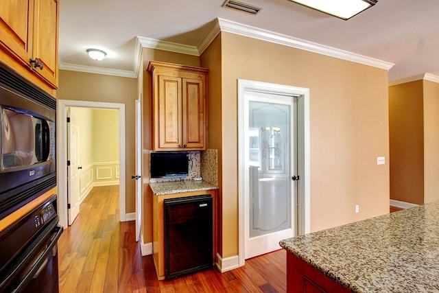 kitchen with dark wood-type flooring, black appliances, crown molding, light stone countertops, and beverage cooler