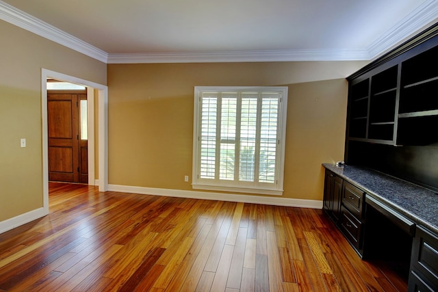 unfurnished living room with wood-type flooring, built in desk, and crown molding