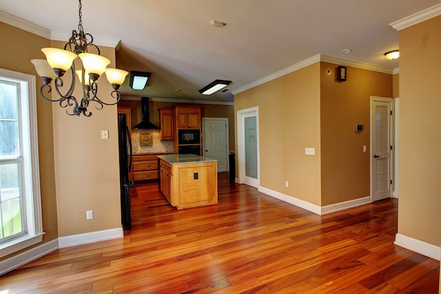 kitchen with a wealth of natural light, a kitchen island, black appliances, and wall chimney range hood