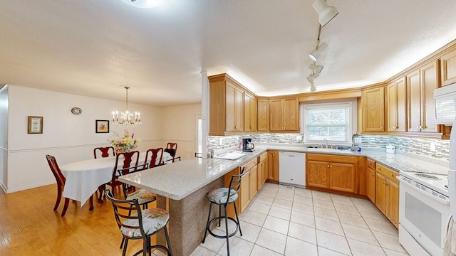 kitchen with a breakfast bar, a sink, backsplash, white appliances, and a peninsula