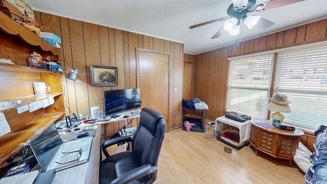 home office featuring a ceiling fan, crown molding, wooden walls, and light wood-style floors