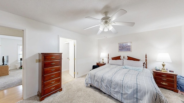 bedroom featuring baseboards, light carpet, a textured ceiling, and ceiling fan