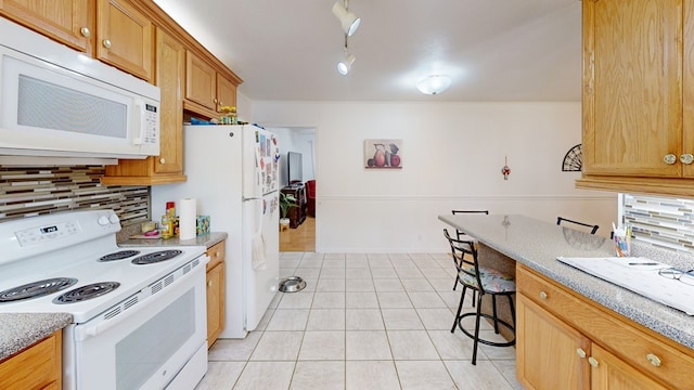 kitchen featuring backsplash, white appliances, light tile patterned flooring, brown cabinetry, and light stone countertops