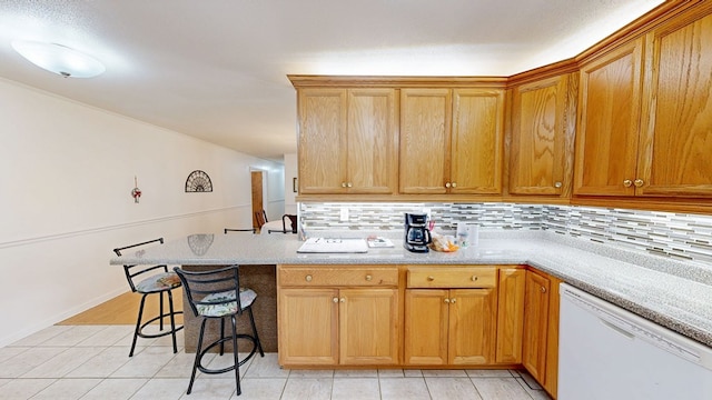 kitchen featuring tasteful backsplash, dishwasher, light countertops, a peninsula, and a kitchen breakfast bar