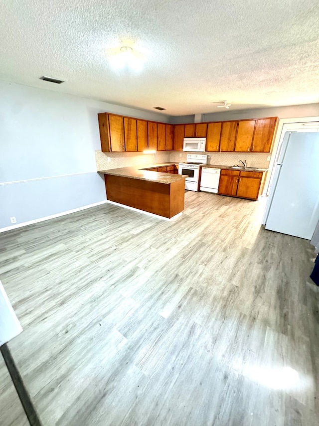 kitchen with a textured ceiling, white appliances, kitchen peninsula, and light hardwood / wood-style flooring