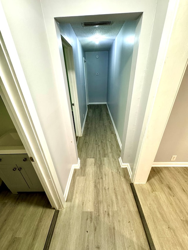 corridor with light wood-type flooring and a textured ceiling