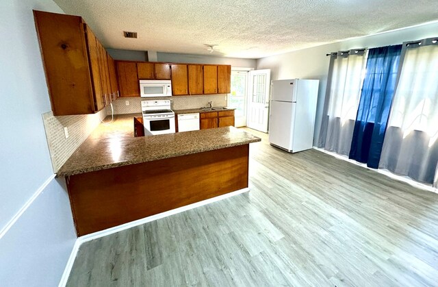 kitchen featuring a textured ceiling, kitchen peninsula, light hardwood / wood-style floors, and white appliances