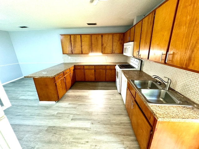 kitchen featuring sink, light hardwood / wood-style flooring, backsplash, kitchen peninsula, and white appliances