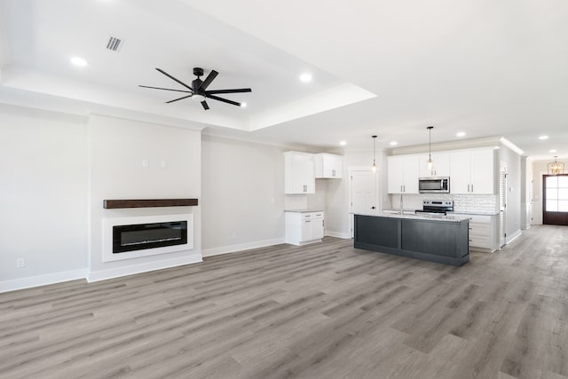 kitchen with a tray ceiling, light countertops, open floor plan, a kitchen island with sink, and white cabinets