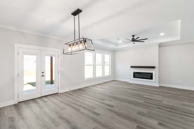 unfurnished living room featuring a tray ceiling, a glass covered fireplace, crown molding, and baseboards