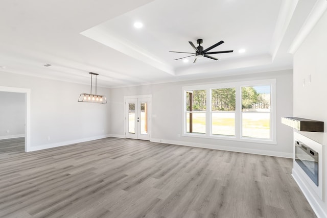 unfurnished living room featuring ornamental molding, a tray ceiling, a glass covered fireplace, and light wood-style flooring