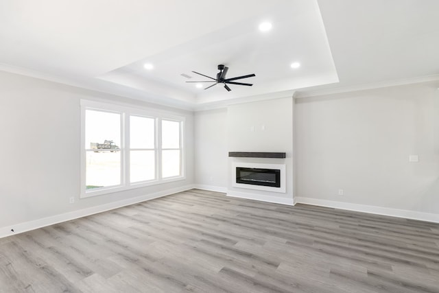 unfurnished living room with ornamental molding, a glass covered fireplace, a raised ceiling, and baseboards