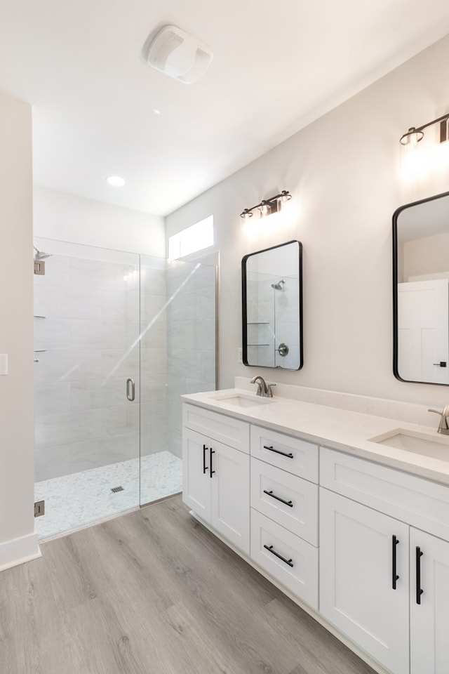 full bathroom with double vanity, a stall shower, a sink, and wood finished floors