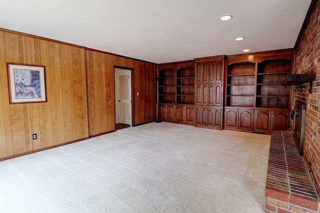 unfurnished living room featuring a brick fireplace, light colored carpet, and wood walls