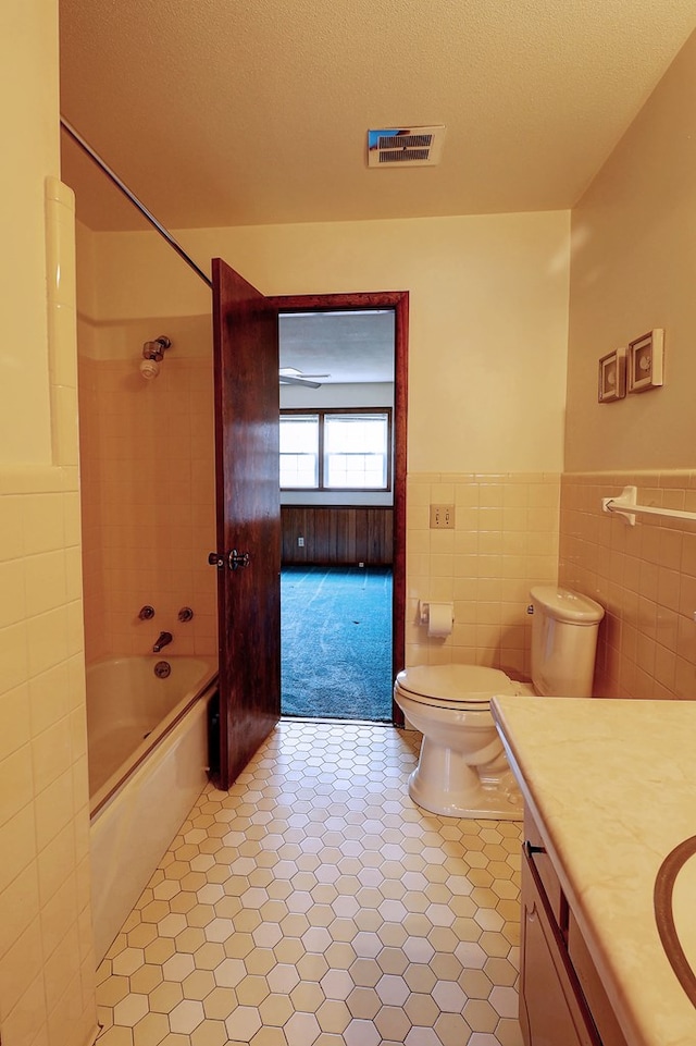 full bathroom featuring toilet, bathing tub / shower combination, a textured ceiling, tile walls, and vanity