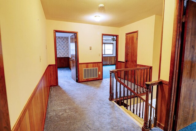 hallway with light colored carpet, a textured ceiling, and wood walls