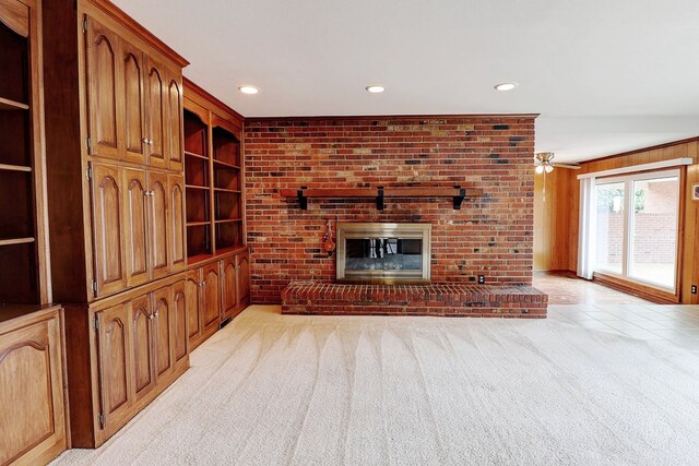 unfurnished living room featuring a brick fireplace, light colored carpet, built in features, and wooden walls