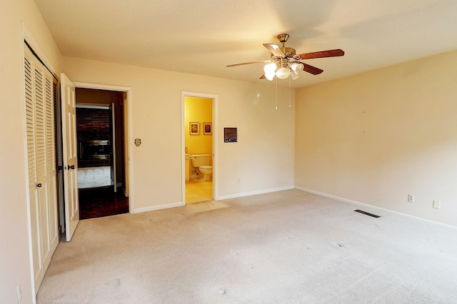 unfurnished bedroom with ceiling fan, light colored carpet, ensuite bath, and a closet