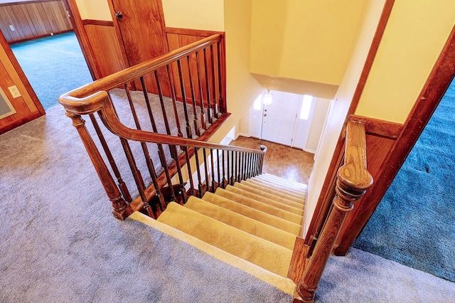 stairs featuring a towering ceiling, carpet floors, and wood walls