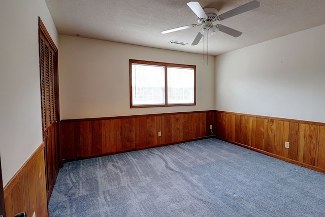 carpeted spare room with ceiling fan, wooden walls, and a textured ceiling