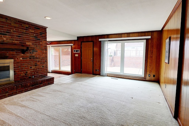 unfurnished living room featuring a brick fireplace, light colored carpet, a healthy amount of sunlight, and wood walls