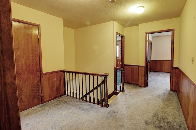 hall with light carpet, wooden walls, and a textured ceiling