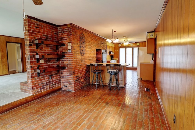 kitchen with ceiling fan with notable chandelier, wood walls, a kitchen bar, stainless steel oven, and kitchen peninsula