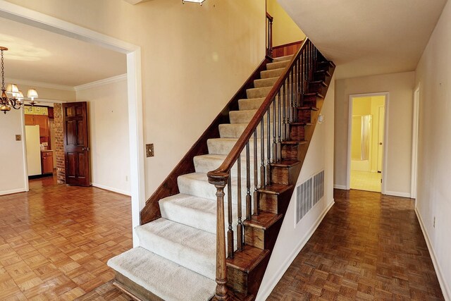 staircase featuring parquet floors, ornamental molding, and a chandelier