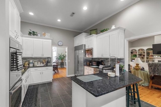 kitchen featuring appliances with stainless steel finishes, backsplash, ornamental molding, a breakfast bar, and white cabinets