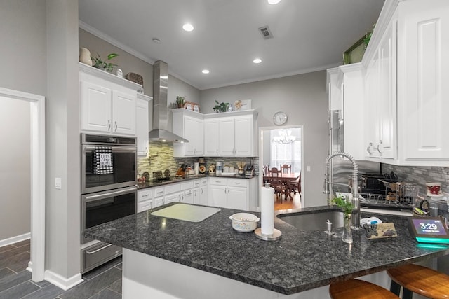 kitchen featuring decorative backsplash, a kitchen breakfast bar, white cabinetry, and wall chimney range hood