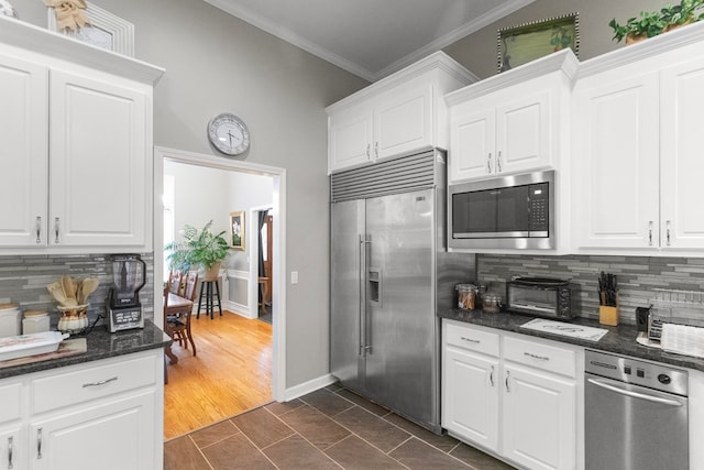 kitchen with built in appliances, decorative backsplash, white cabinetry, and ornamental molding