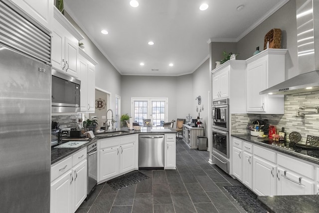 kitchen with kitchen peninsula, tasteful backsplash, wall chimney exhaust hood, built in appliances, and white cabinets