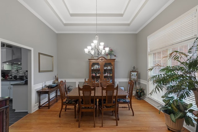 dining room featuring a tray ceiling, crown molding, wood-type flooring, and a notable chandelier