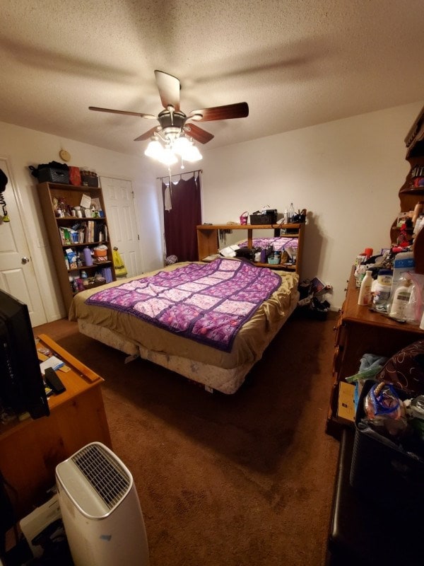 bedroom with ceiling fan, a textured ceiling, and dark colored carpet
