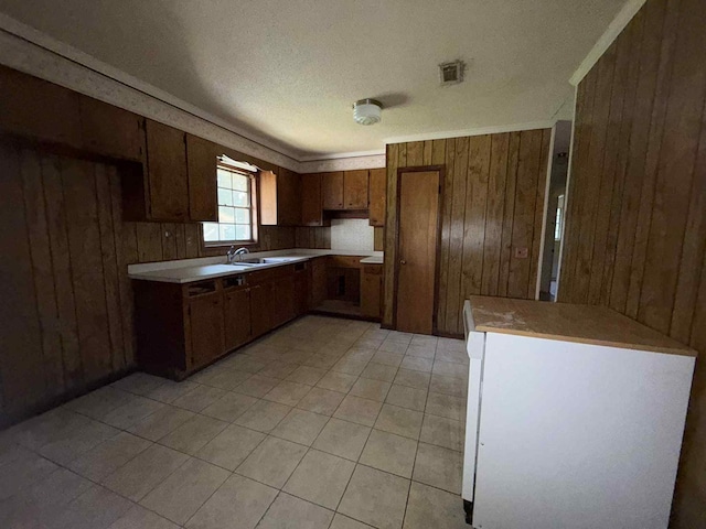 230 Sharon Ct, Ozark, AL 36360 - kitchen with wood walls, brown cabinetry, light countertops, light tile patterned floors, and crown molding