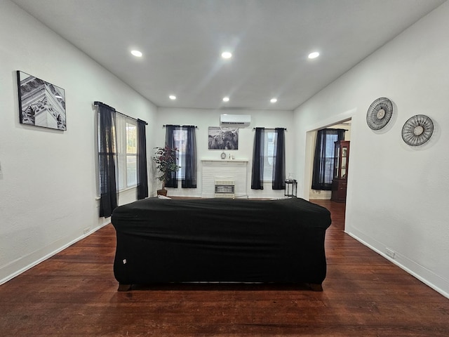 living room featuring wood finished floors, baseboards, a wall mounted AC, recessed lighting, and a brick fireplace