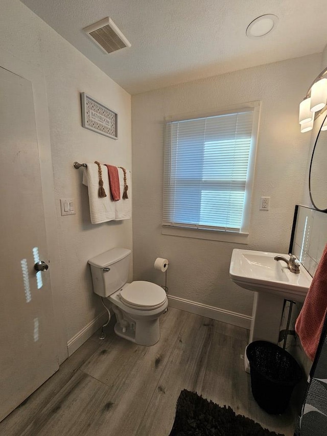 half bath with visible vents, baseboards, toilet, wood finished floors, and a textured ceiling