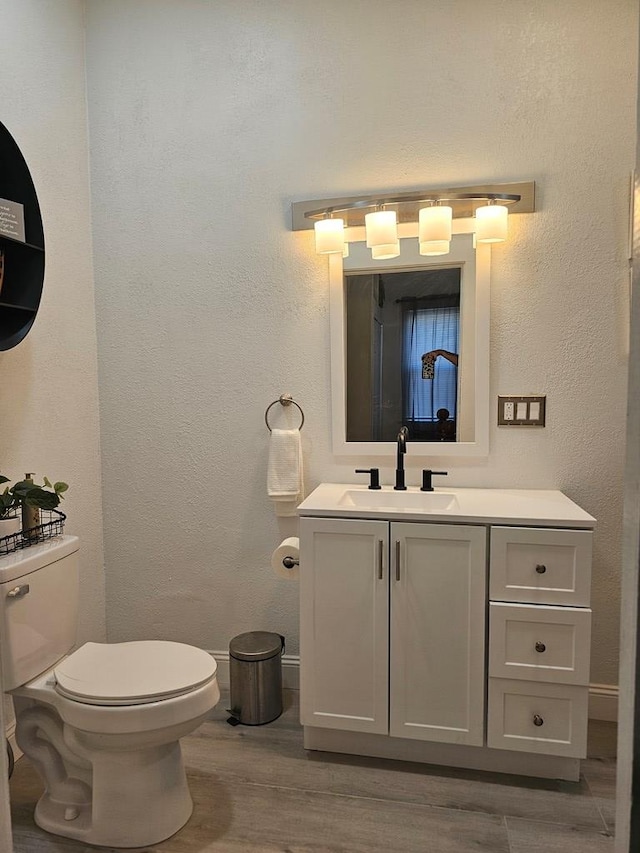 bathroom featuring baseboards, toilet, wood finished floors, a textured wall, and vanity