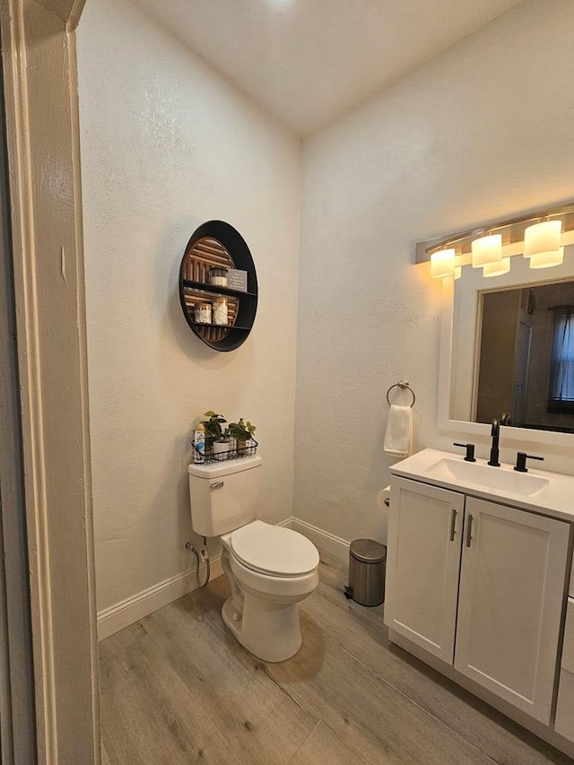 half bath with toilet, vanity, baseboards, and wood finished floors