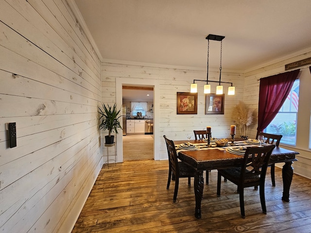 dining space with crown molding, wood-type flooring, and wooden walls