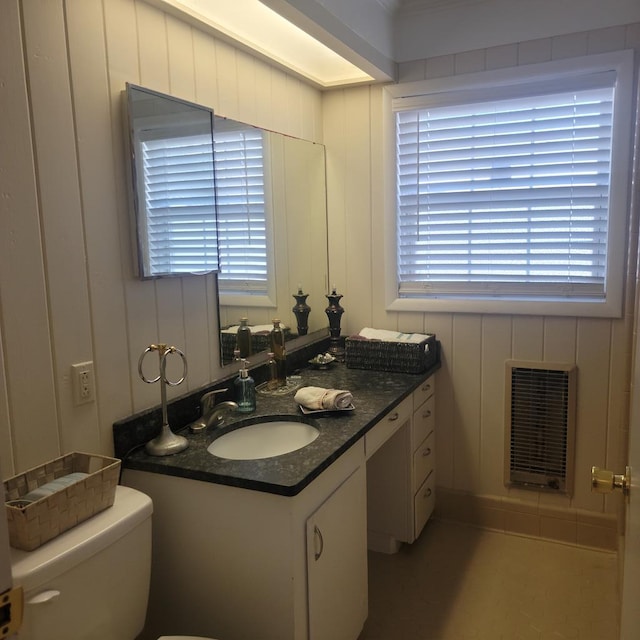 half bathroom featuring vanity, toilet, heating unit, and a wealth of natural light