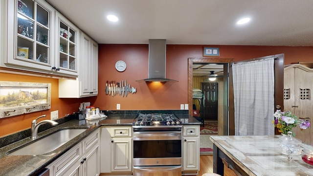 kitchen featuring sink, stainless steel gas stove, white cabinetry, and wall chimney exhaust hood