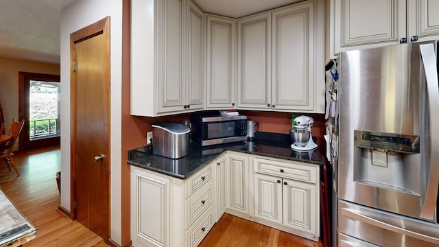 kitchen featuring stainless steel appliances, light hardwood / wood-style floors, and dark stone countertops