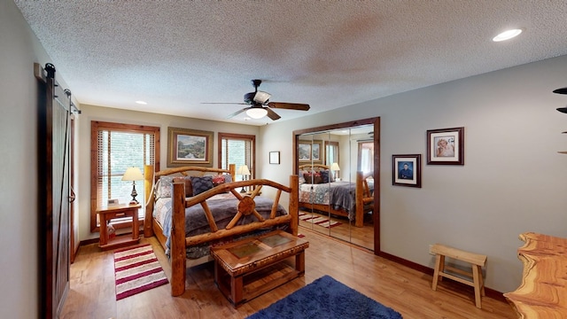 bedroom with a textured ceiling, a closet, hardwood / wood-style floors, a barn door, and ceiling fan