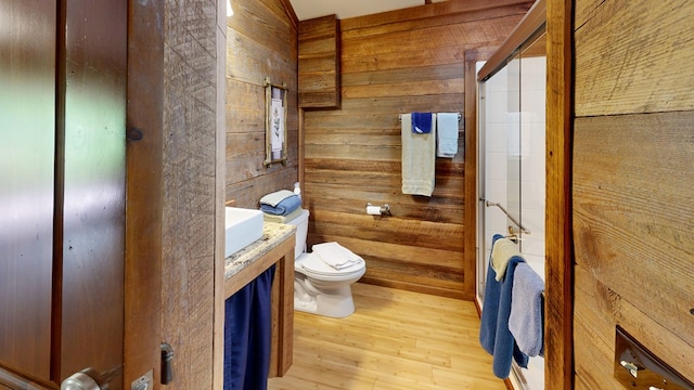 bathroom with hardwood / wood-style floors, toilet, wooden walls, and vanity