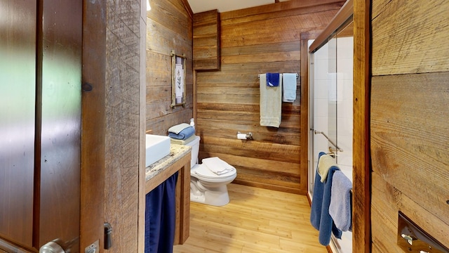 full bathroom with wood walls, toilet, wood finished floors, an enclosed shower, and vanity