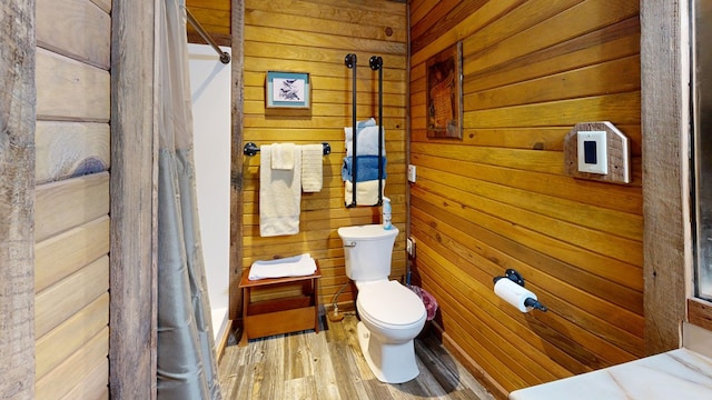 bathroom with toilet, a shower with shower curtain, wooden walls, and hardwood / wood-style floors